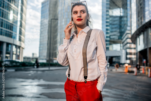 Business Woman With Phone Near Office. Portrait Of Beautiful Smiling Female In Fashion Office Clothes Talking On Phone While Standing Outdoors. Phone Communication. High Quality Image © Kirill