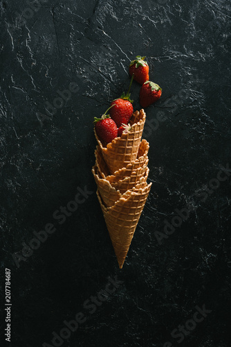 Ripe strawberries in stacked waffle cones on dark background