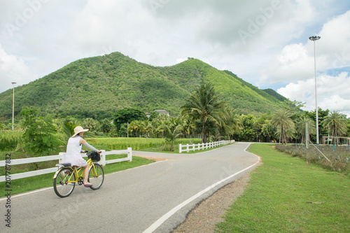Asian woman having fun and smiling riding bicycle on the road in cloudy day (Mountain background) © 9kwan