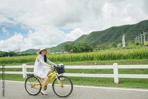 Asian woman having fun and smiling riding bicycle on the road in cloudy day (Mountain background)