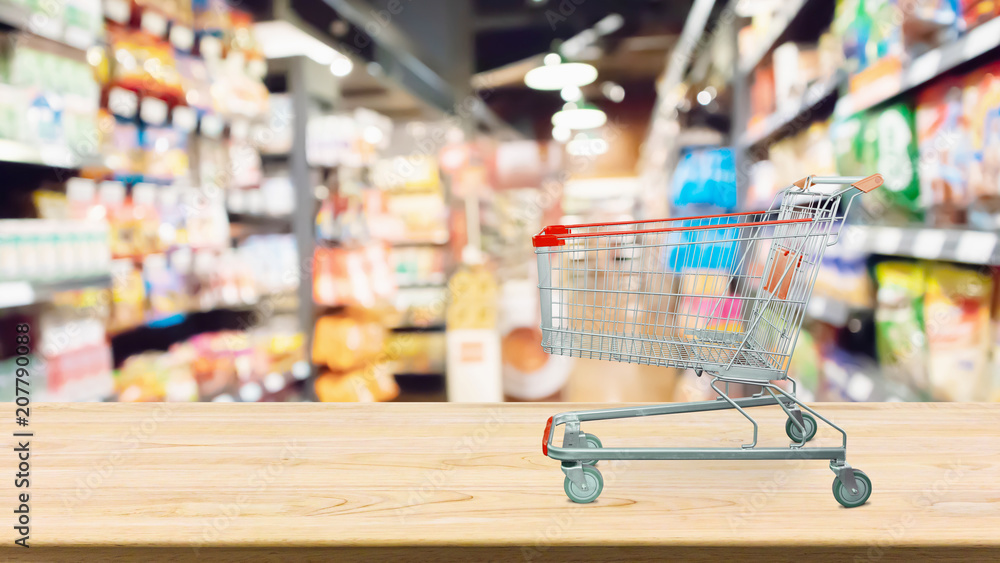 Abstract blur supermarket shelves defocused background with shopping cart on wood table