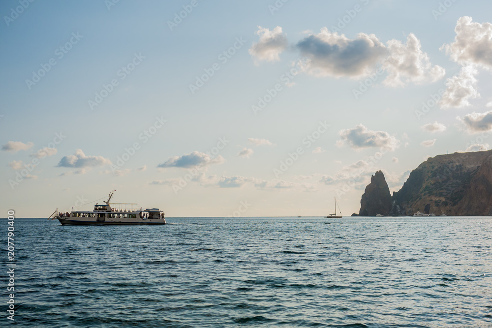 the rocky shore. high rocky cliff and boat at sea. summer evening