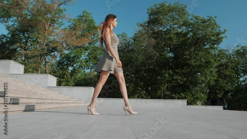 Sexy legs with high beige heels goes down the stairs of big city. Roamntic woman walking on boulvard alone. Attractive girl in short dress at summer season. Slow motion. photo