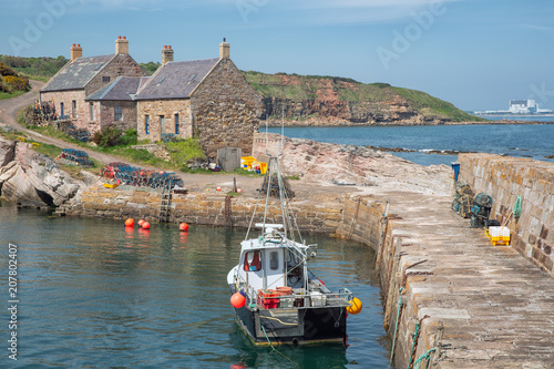Cove harbor with fishing ship at Scottish North sea coast. At the background Torness Nuclear Power Station