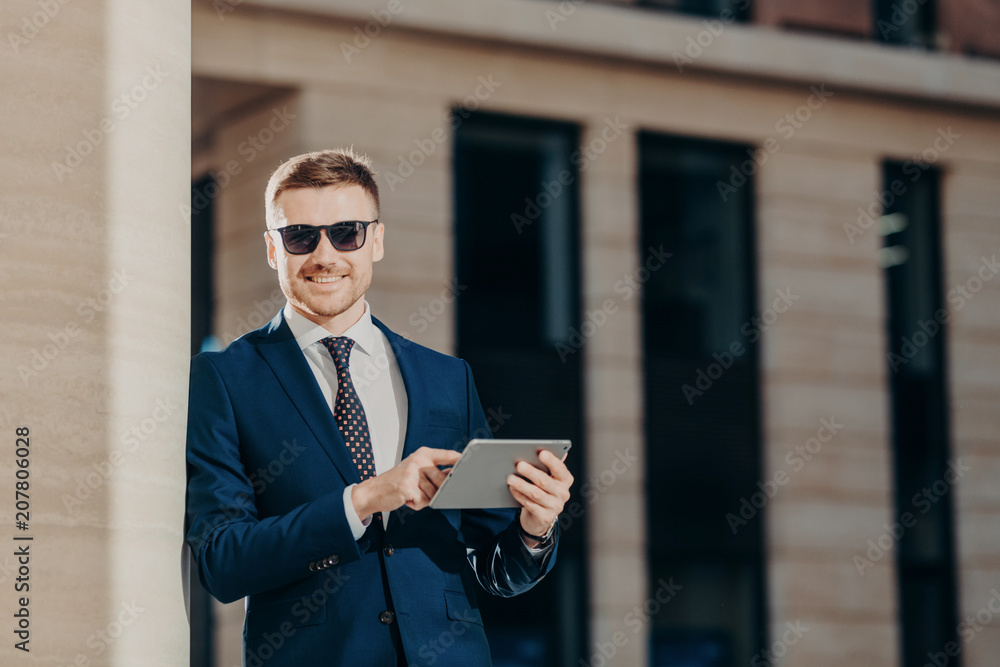 Stylish business owner in trendy sunglasses uses modern digital tablet for taking part in online conference with business partners, has positive smile on face, connected to wireless internet Stylish business owner in trendy sunglasses uses modern digital tablet for taking part in online conference with business partners, has positive smile on face, connected to wireless internet