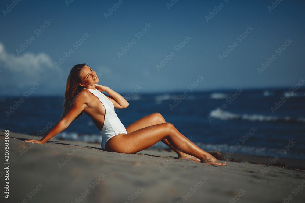 Young woman posing on the beach in a white swimsuit