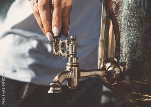 The girl's hand turns the tap of the old samovar