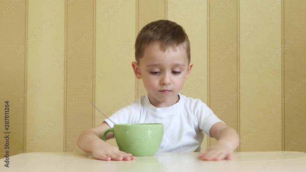 The child with pleasure and with a smile eats soup from a green plate, sitting at a table. The child with pleasure and with a smile eats soup from a green plate, sitting at a table.