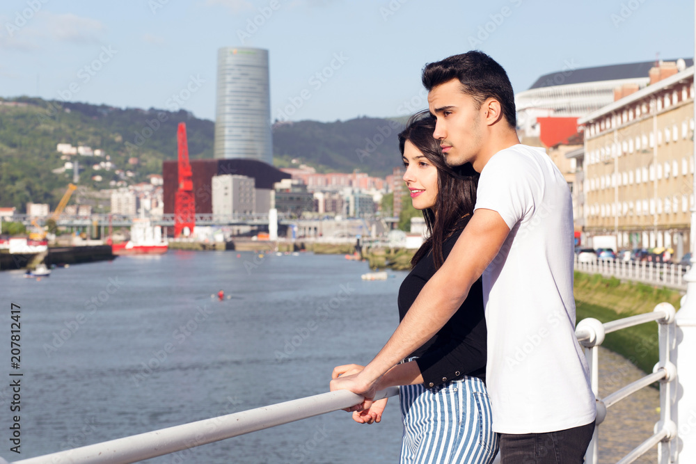 Young couple in love near the river of Bilbao, Spain. Outdoors, on a sunny day.