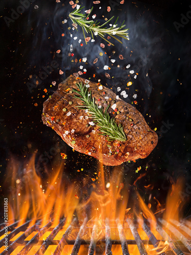 Tasty beef steak flying above cast iron grate with fire flames.