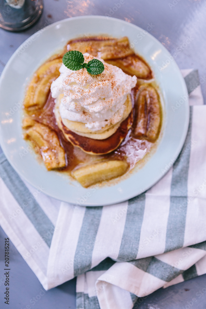 Top view of Pancakes with caramel-banana syrup topping with whip cream and mint leaves. In blue plate over fabric with blue stripes.