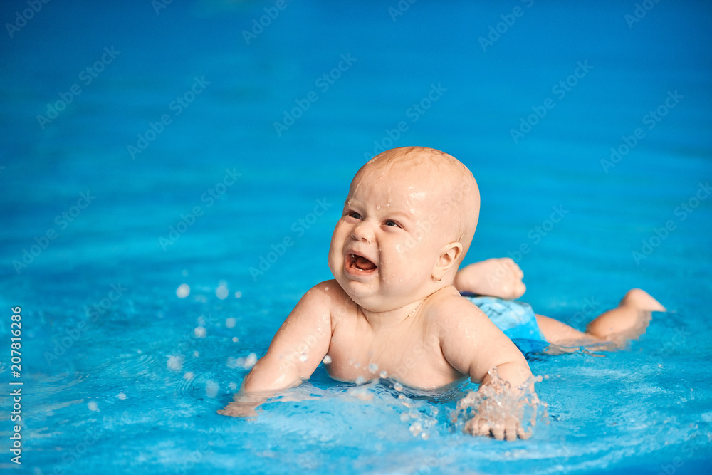Funny little baby boy lying in blue pool. Active lifestyle of child.
