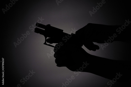 black silhouette of a male reloading a gun in the dark