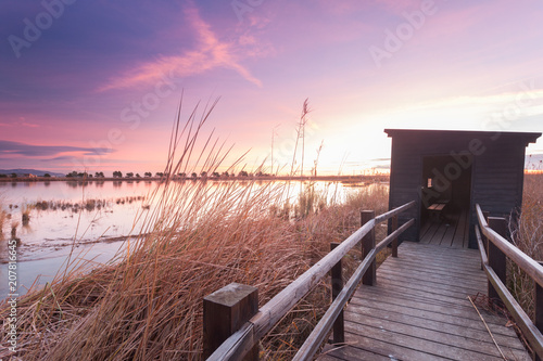 Holzsteg zu einer Beobachtungshütte für Vogelbeobachtung im Ebro Delta nahe Barcelona am Morgen zu Sonnenaufgang