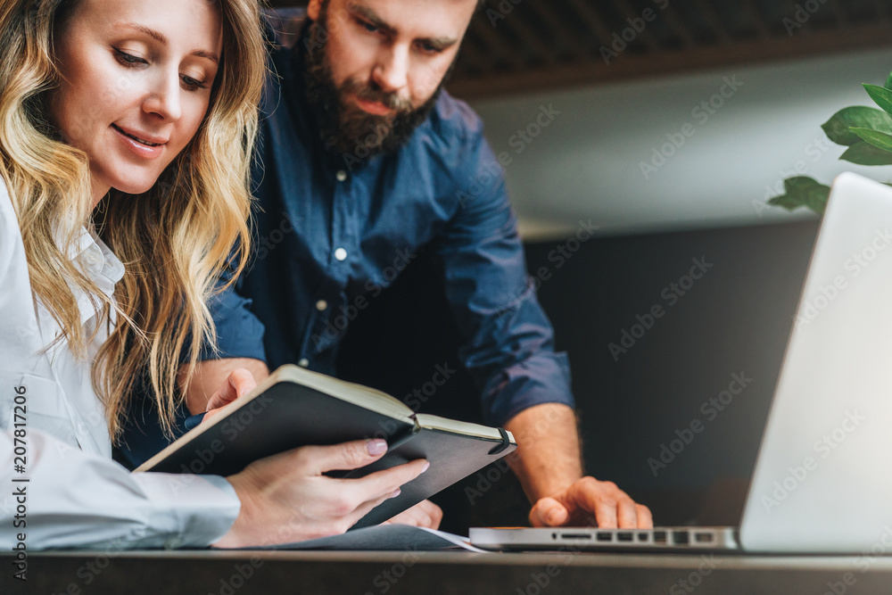 Business meeting. Teamwork. Smiling businesswoman and businessman sitting at table in front of laptop and working. Beautiful woman shows a man writing in notebook. Education, learning, distance work. Business meeting. Teamwork. Smiling businesswoman and businessman sitting at table in front of laptop and working. Beautiful woman shows a man writing in notebook. Education, learning, distance work.
