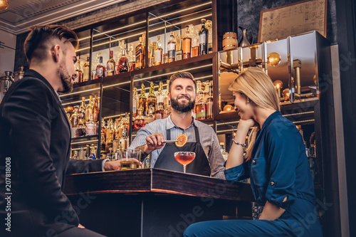 Cheerful stylish brutal barman serves an attractive couple who spend an evening on a date.