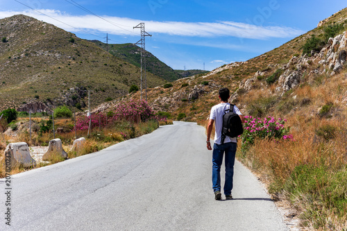 Hombre caminando por una carretera en medio de una montaña con una mochila al hombro