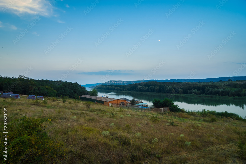 House on the water, against the background of the Dniester and fjords with trees on the shore. Summer evening, evening sunrise. Bakota, Ukraine.