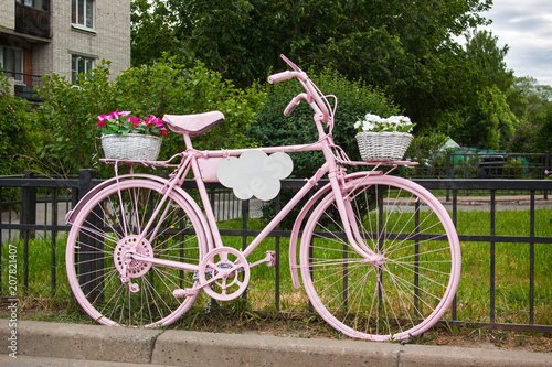 Pink bicycle with flowers baskets long standing next to the fence