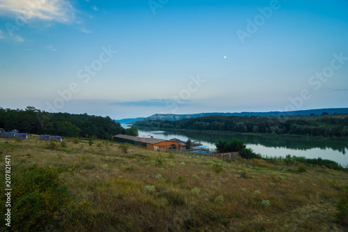 House on the water, against the background of the Dniester and fjords with trees on the shore. Summer evening, evening sunrise. Bakota, Ukraine.