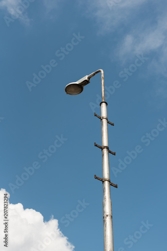 Old industrial street lamp against blue sky with white clouds.