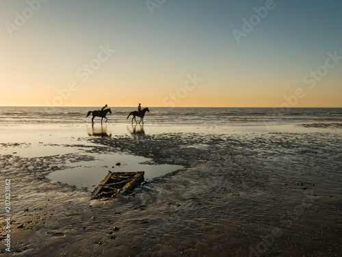 Two horseback riders taking a ride at sunset at an empty beach