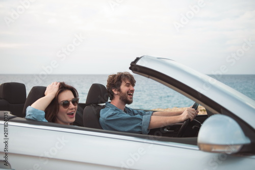 Happy together. Cheerful young couple in love is driving car with open roof while travelling along seaboard. They are enjoying romantic vacation abroad. Family trip concept © Yakobchuk Olena