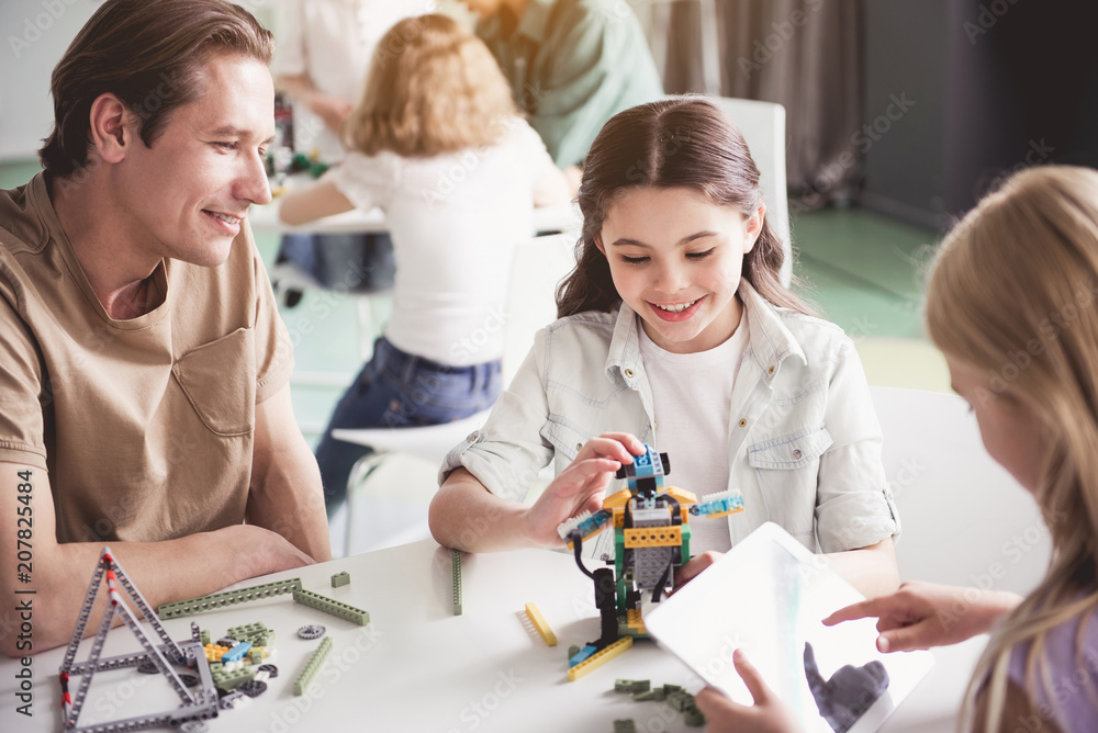 Fototapeta premium Cheerful kids and outgoing man creating robot from constructor during lesson