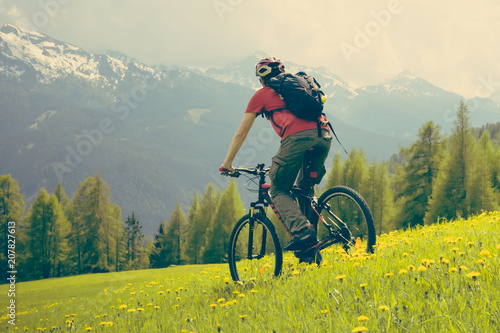 MTB bicycle ride in the mountain meadow, rear view of cyclist in helmet, summer haze