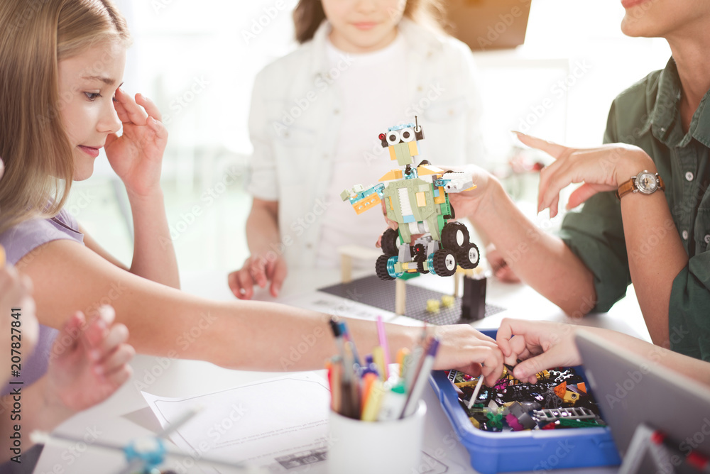Outgoing children having fun with robot. They creating it from constructor while taking details from box. Modern education concept Outgoing children having fun with robot. They creating it from constructor while taking details from box. Modern education concept