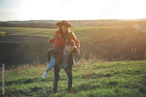 Happy in love. Full length of full of happiness and joy couple in summer evening nature. Boy is carrying girl with cellphone in hand. They are smiling and having fun together