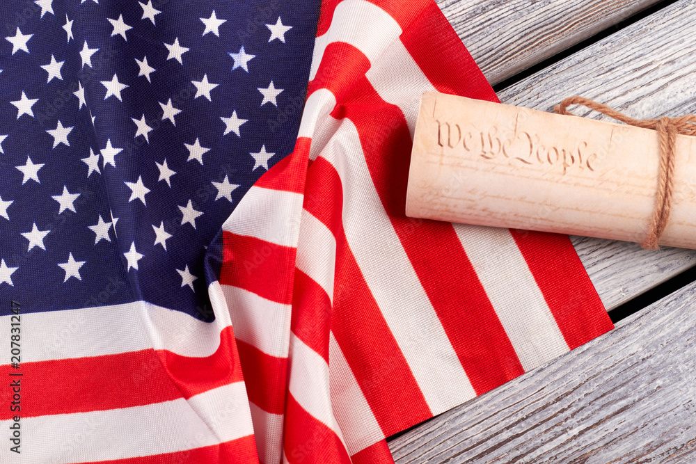 Obraz premium Constitution of the US and USA flag. American flag with rolled-up of constitution document on wooden table.