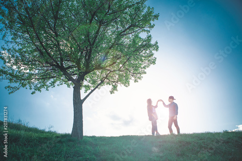 Always in my mind. Full length of loving boy and girl making heart by their fingers on bright sun behind. They are standing on pictorial hill among colourful summer beauty