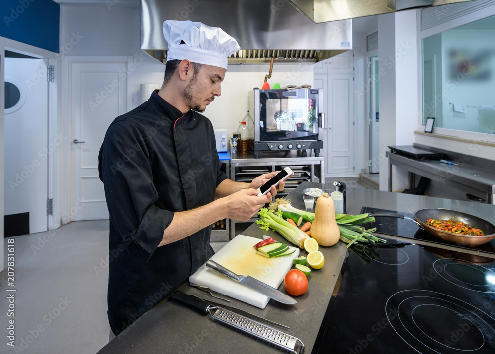 young chef by referring to a Smartphone or tablet in a professional kitchen young chef by referring to a Smartphone or tablet in a professional kitchen