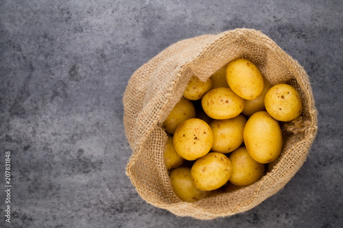 Sack of fresh raw potatoes on wooden background, top view