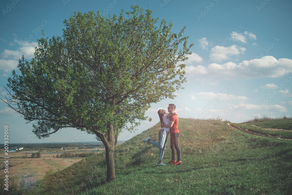 My summer love. Full length of female and her boyfriend hugging and smiling near tree. Young woman raising leg in excitement and laughing