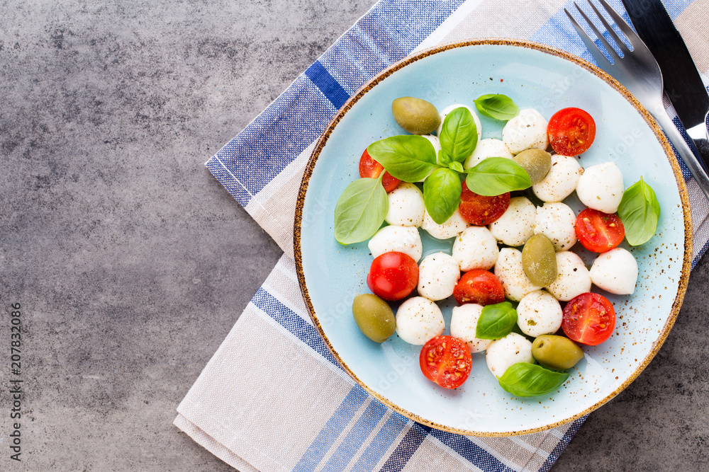 Delicious caprese salad with ripe cherry tomatoes and mini mozzarella cheese balls with fresh basil leaves. Delicious caprese salad with ripe cherry tomatoes and mini mozzarella cheese balls with fresh basil leaves.