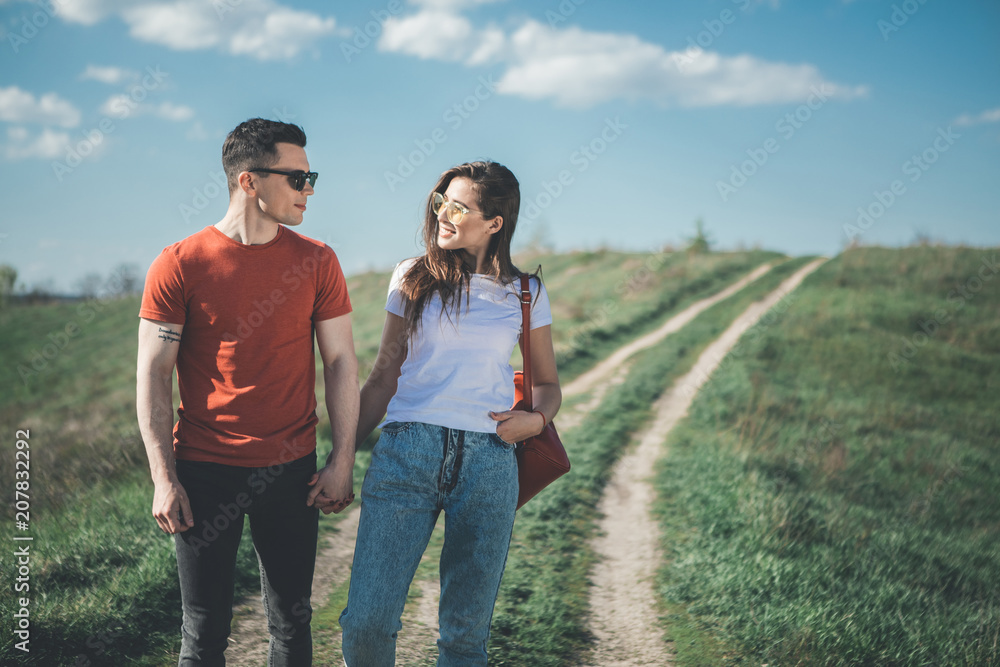 Falling in love. Full length of amorous young man and woman holding hands while strolling in nature. They are looking at each other with smile and affection. Copy space in right side Falling in love. Full length of amorous young man and woman holding hands while strolling in nature. They are looking at each other with smile and affection. Copy space in right side