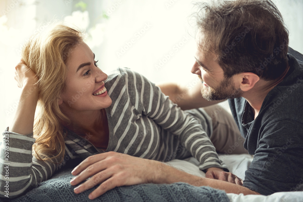 Cheerful bearded man is embracing beloved woman. She is looking at soulmate with love and joy. They are lying on couch in domestic atmosphere an enjoying themselves Cheerful bearded man is embracing beloved woman. She is looking at soulmate with love and joy. They are lying on couch in domestic atmosphere an enjoying themselves