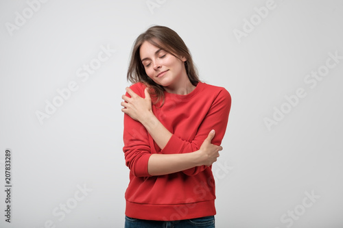 Fotografía Portrait of a pretty young girl in red shirt hugging herself