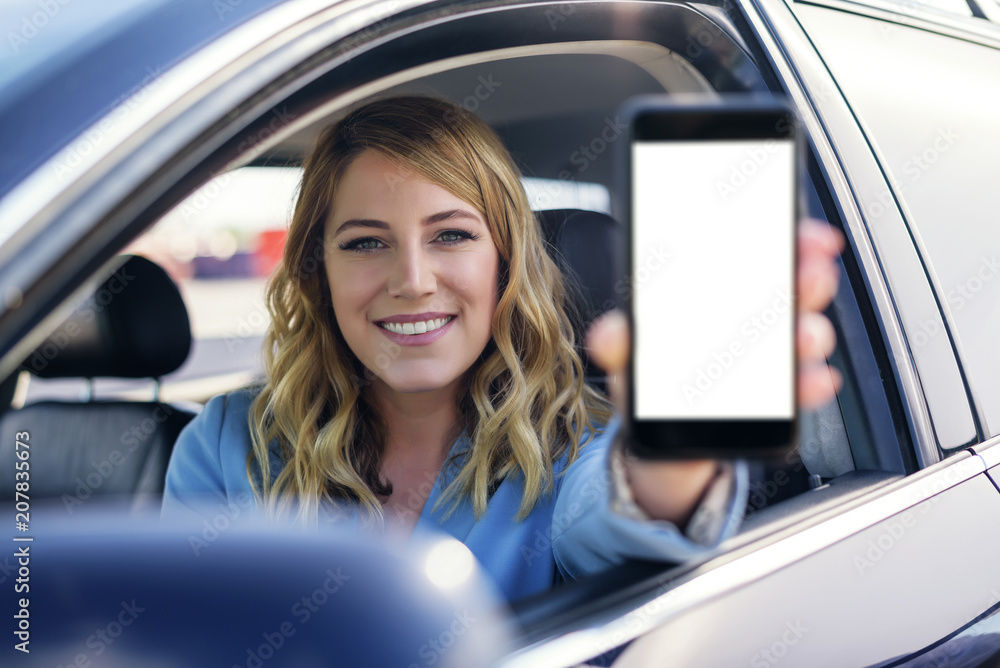 Young woman in auto shows smartphone with blank screen.