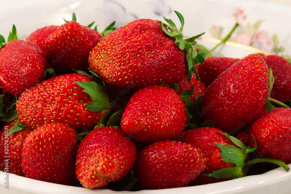 A large ripe strawberry with green leaves, stacked with a slide in a plate. A large ripe strawberry with green leaves, stacked with a slide in a plate.