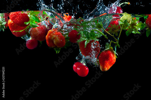 Red strawberries and cherries dropped into the water with splash on a black background