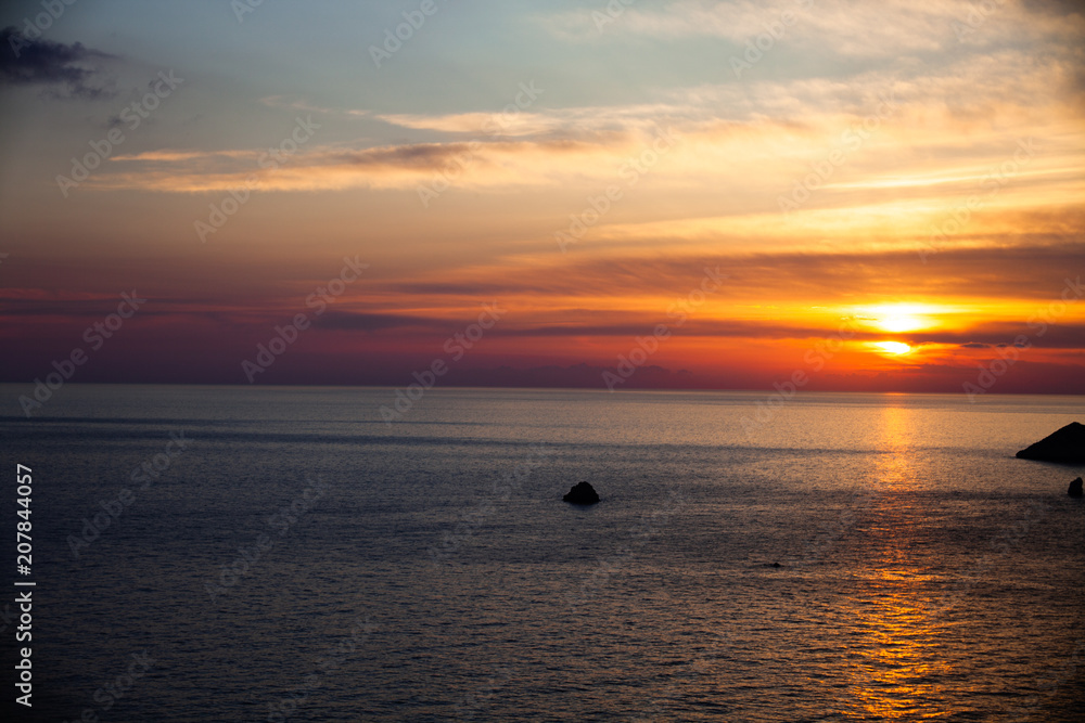 Sunset on the beach with clouds. Calm sea water. Beautiful colors in the sky. Blue and orange shades. Quiet place. Relaxing scene of beaches. Pretty natural landscape
