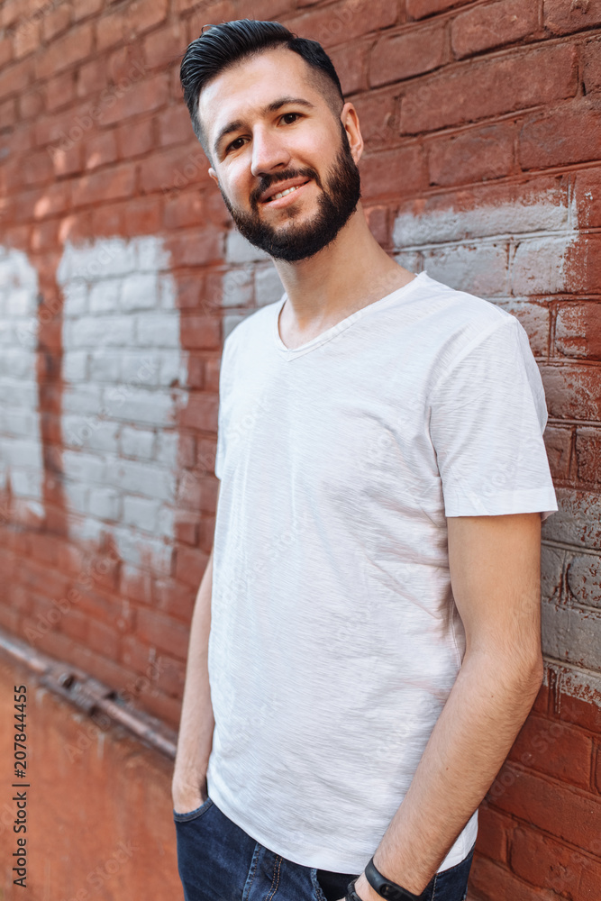 Portrait of a stylish and positive Guy, in a white empty t-shirt, against the orange brick wall, can be used for advertising, text insertion