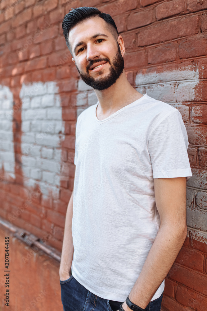 Portrait of a stylish and positive Guy, in a white empty t-shirt, against the orange brick wall, can be used for advertising, text insertion Portrait of a stylish and positive Guy, in a white empty t-shirt, against the orange brick wall, can be used for advertising, text insertion