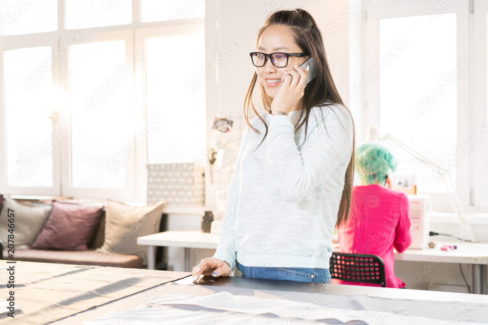 Portrait of Asian young woman speaking by phone while working in modern atelier, copy space Portrait of Asian young woman speaking by phone while working in modern atelier, copy space