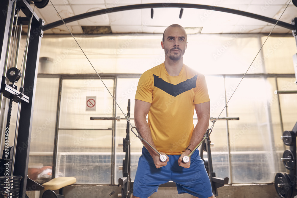 one young man, serious expression, wearing sport clothes, exercise on resistance bands, in old beaten up gym interior.western shot. one young man, serious expression, wearing sport clothes, exercise on resistance bands, in old beaten up gym interior.western shot.