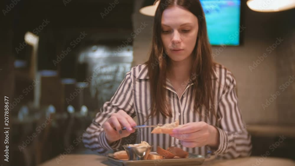 Young beautiful woman brunette smears pate on a piece of bread in cafe with knife. And she eats sandwich. Young beautiful woman brunette smears pate on a piece of bread in cafe with knife. And she eats sandwich.