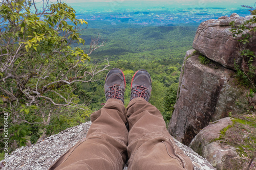 Legs of a men resting in boots for mountain tracking against the backdrop of mountains and valleys with noisy clouds Hiking boots in the mountains. Resting time. Freedom concept